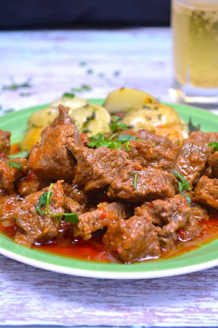 Serving Authentic Hungarian beef paprikash with tender beef cubes and rich red sauce on a green plate with potatoes.