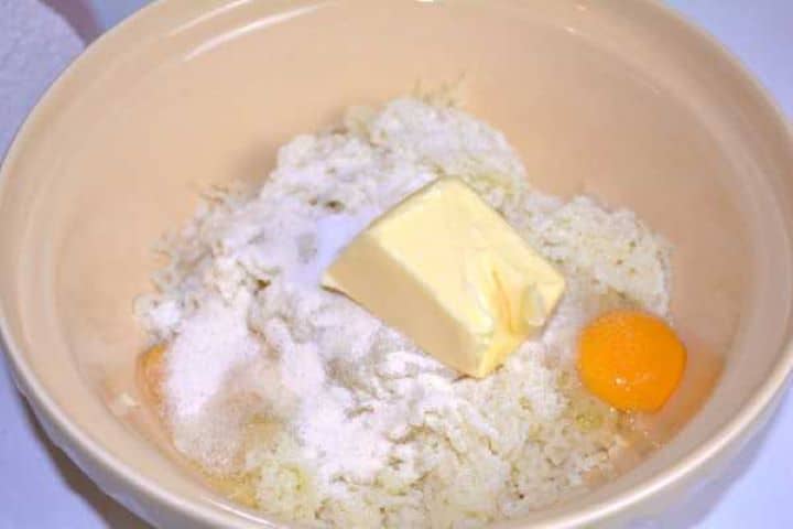 Ingredients in Bowl Adding room-temperature eggs, butter, salt, and coarse semolina to cooled riced potatoes.