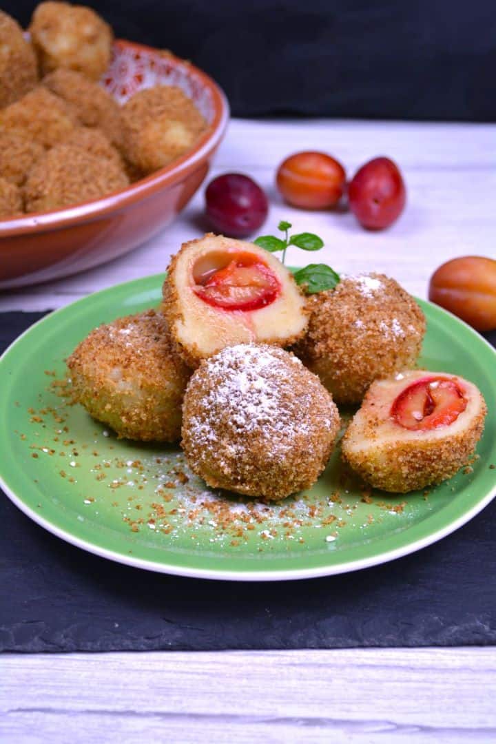 Authentic Hungarian plum dumplings (szilvás gombóc) coated in toasted breadcrumbs and dusted with vanilla sugar on a green plate.