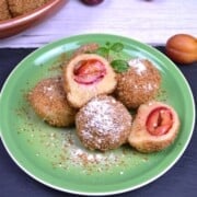 Authentic Hungarian plum dumplings (szilvás gombóc) coated in toasted breadcrumbs and dusted with vanilla sugar on a green plate.