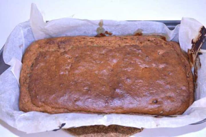 Ready Golden brown freshly baked no added sugar banana bread cooling inside a parchment lined loaf pan.