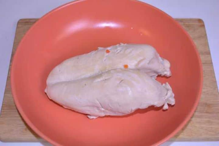 Chicken Breast Tender boiled chicken breast resting on an orange plate to cool before deboning.