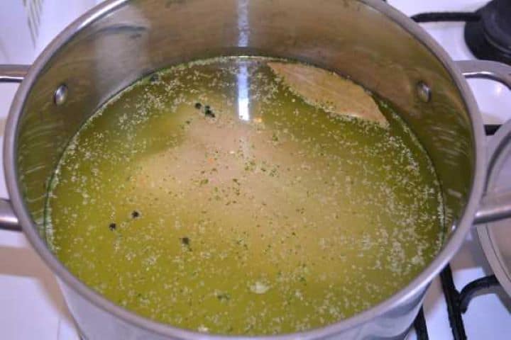 Boiling Poaching bone-in chicken breast in a soup pot with water, dried vegetable mix, peppercorns, and bay leaf.