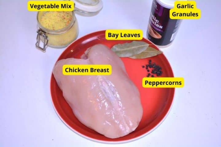 Ingredients For Boiling Raw bone-in chicken breast, bay leaves, peppercorns, dried vegetable soup mix, and garlic granules arranged on a prep board.