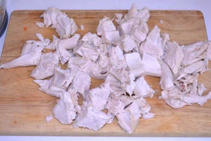 Cut Meat Cooked boneless chicken breast chopped into rough chunks on a wooden cutting board.