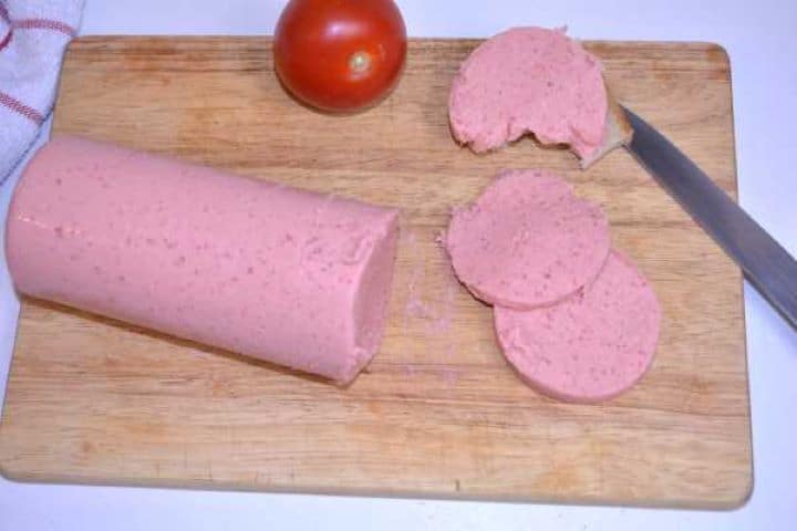 Served Rustic wooden board loaded with sliced chicken salami, fresh crusty bread, and ripe red tomatoes for a healthy breakfast spread.