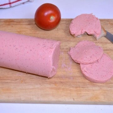 Thin slices of homemade chicken salami served with fresh red tomatoes on a wooden chopping board.