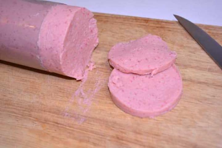 Slicing Firm, chilled homemade chicken salami roll unmolded from the bottle mold and sliced on a cutting board.