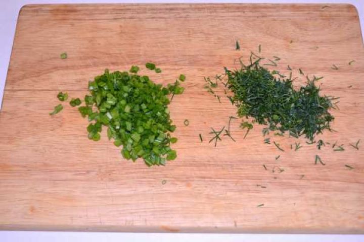 Chopped Finely chopped fresh dill and chives on a wooden cutting board for seasoning the fish spread.