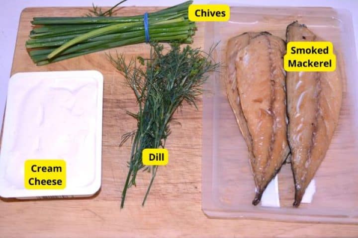 Ingredients Ingredients for smoked mackerel spread including hot-smoked mackerel fillets, full-fat cream cheese, fresh dill, and chives on a wooden cutting board.