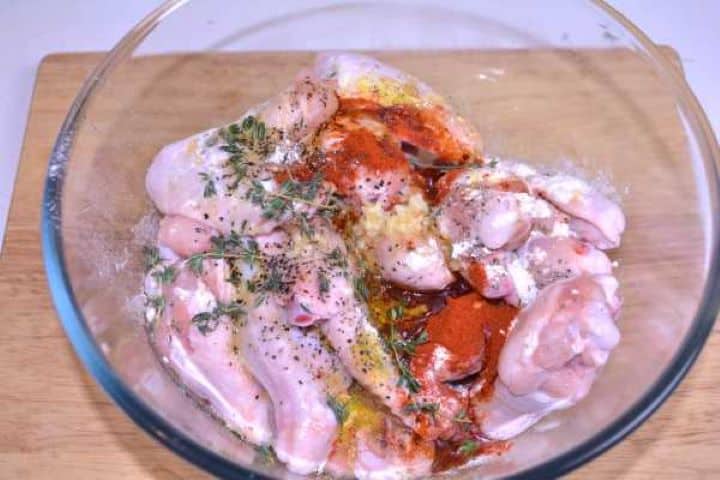 All in Bowl Fresh chicken wings in a glass bowl with paprika, crushed garlic, olive oil, and herbs ready to mix.