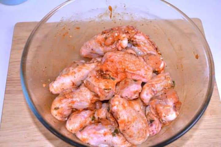 Raw chicken wings coated and thoroughly massaged with honey garlic paprika marinade in a glass bowl.