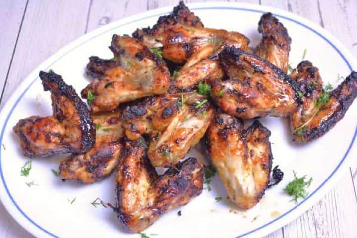 Serve Serving platter of sticky glazed honey garlic chicken wings garnished with fresh chopped herbs.