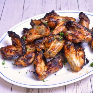 Crispy air fryer honey garlic chicken wings served on a white plate with fresh parsley garnish.