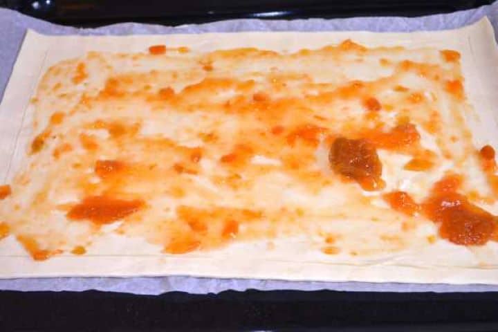 Jam Spread Apricot jam spread evenly over a sheet of puff pastry inside the scored border on baking parchment.