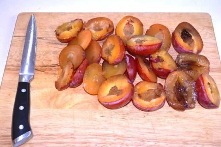 Pitted Plums Washed and pitted fresh plum halves arranged on a wooden chopping board.