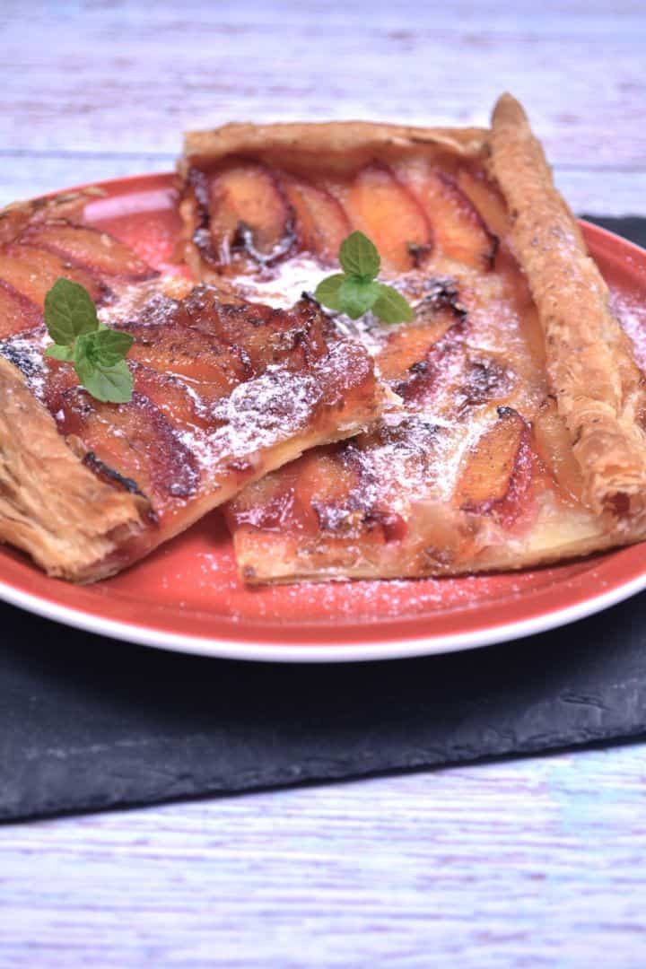Serving Freshly baked puff pastry plum tart with golden flaky crust and caramelized plums served on a red plate.
