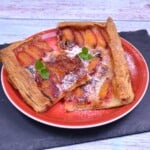Freshly baked puff pastry plum tart with golden flaky crust and caramelized plums served on a red plate.