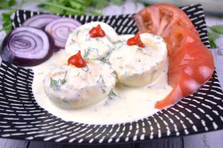 Served Transylvanian style deviled eggs without vinegar arranged on a black plate with fresh spring vegetables.