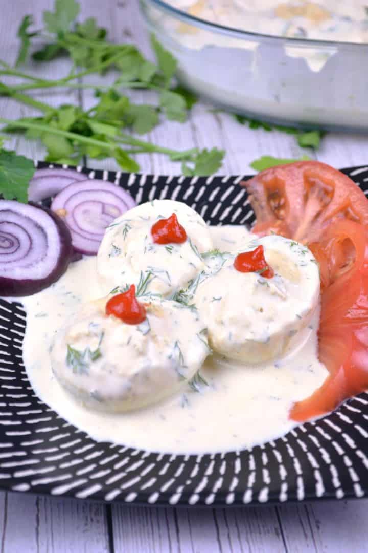 Serving Platter of creamy deviled eggs without vinegar topped with dill and served with sliced tomatoes and onions.