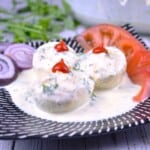 Platter of creamy deviled eggs without vinegar topped with dill and served with sliced tomatoes and onions.