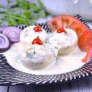 Platter of creamy deviled eggs without vinegar topped with dill and served with sliced tomatoes and onions.