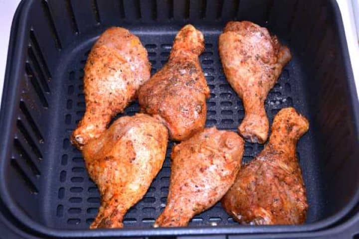 Basket Raw seasoned chicken drumsticks spaced out in a single layer inside a Cosori air fryer basket.