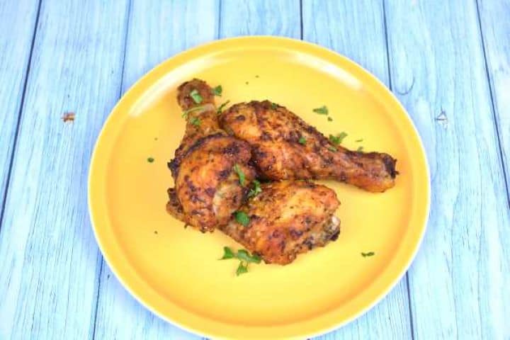 Golden air fryer chicken drumsticks arranged on a yellow ceramic plate garnished with fresh parsley.