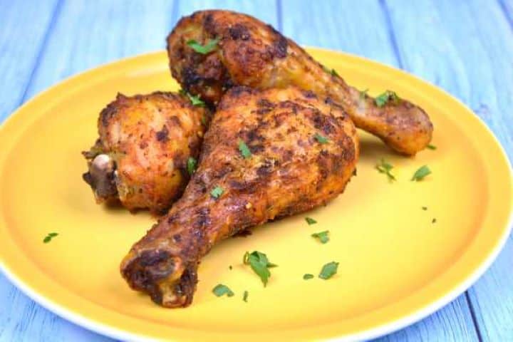 Served Three crispy seasoned chicken drumsticks cooked in an air fryer stacked on a yellow plate.