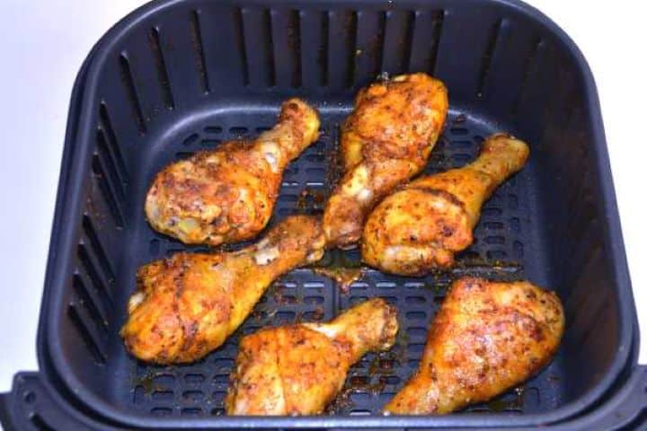 Half-fried Halfway cooked chicken drumsticks turned over in the air fryer basket showing lightly browned skin.