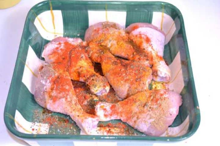 Seasoning Massaging olive oil, Hungarian paprika, and dried herbs into raw chicken drumsticks in a bowl.