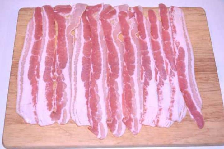 Bacon Slices of smoked streaky bacon laid out flat and overlapping on a wooden board.