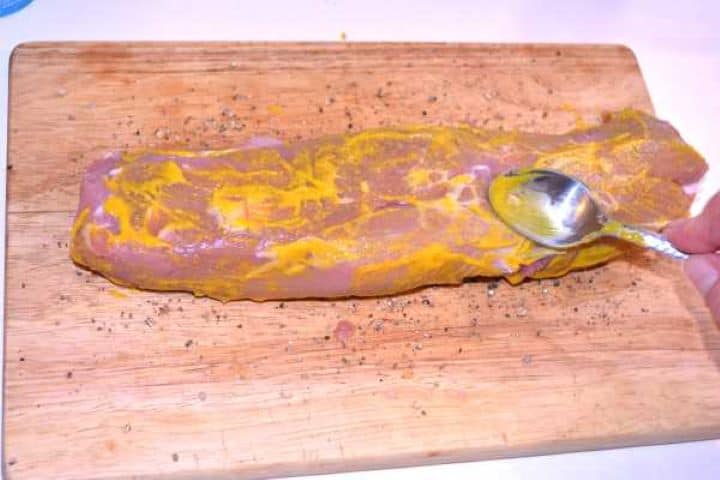 Tenderloin Raw pork tenderloin coated in English mustard and black pepper on a cutting board.