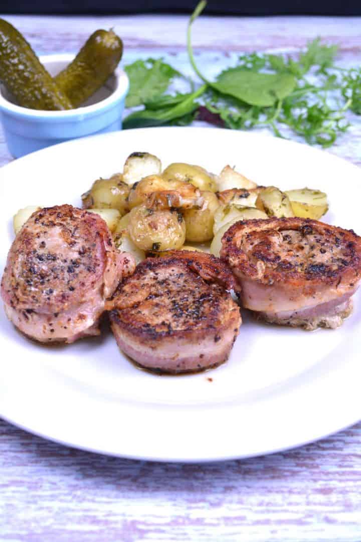 Serving Juicy pan-seared bacon-wrapped pork medallions served on a white plate with buttery parsley potatoes.