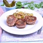 Juicy pan-seared bacon-wrapped pork medallions served on a white plate with buttery parsley potatoes.