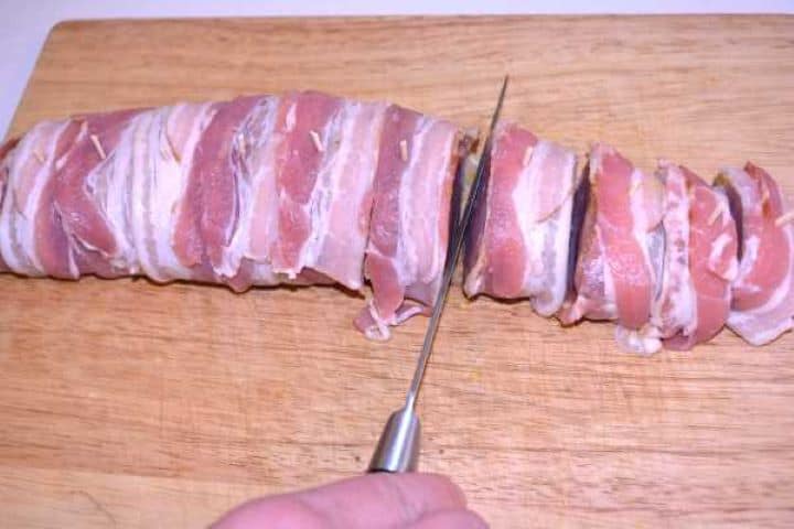 Slicing Slicing bacon-wrapped pork tenderloin into individual medallions with a sharp chef knife.