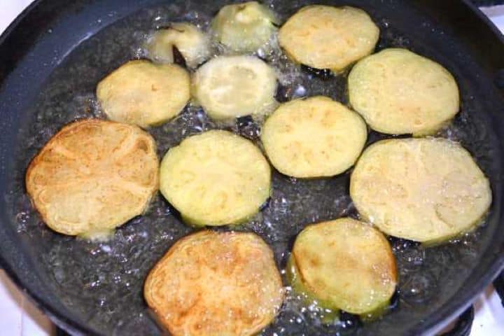 Frying Shallow frying sliced aubergine rounds in hot oil until golden brown on both sides.