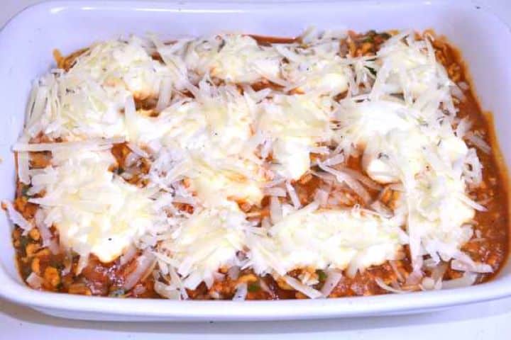 Top Topping the Greek yogurt layer with freshly grated Manchego cheese before baking.