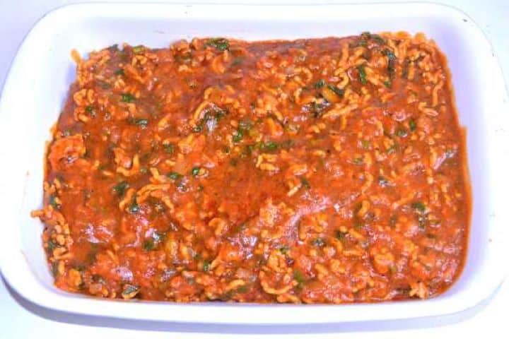 Second Spreading the rich spiced pork and tomato passata sauce evenly over the aubergines in the baking dish.