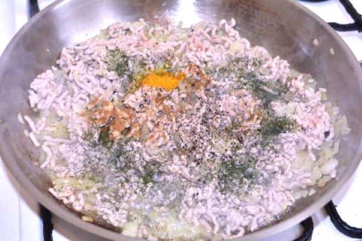 Seasoning Adding ground turmeric, ginger powder, dried dill, and black pepper to browned minced meat in the pan.