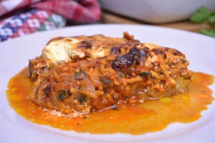 Served Close-up view of Turkish aubergine moussaka highlighting the melting aubergine texture, rich paprika meat gravy, and melted Manchego topping.