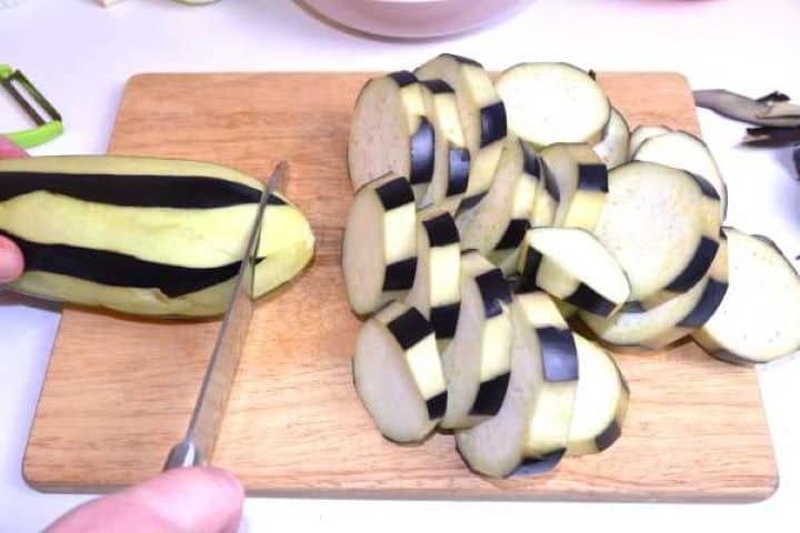 Slicing Peeling fresh aubergines in alternating zebra stripes using a vegetable peeler for Turkish moussaka.