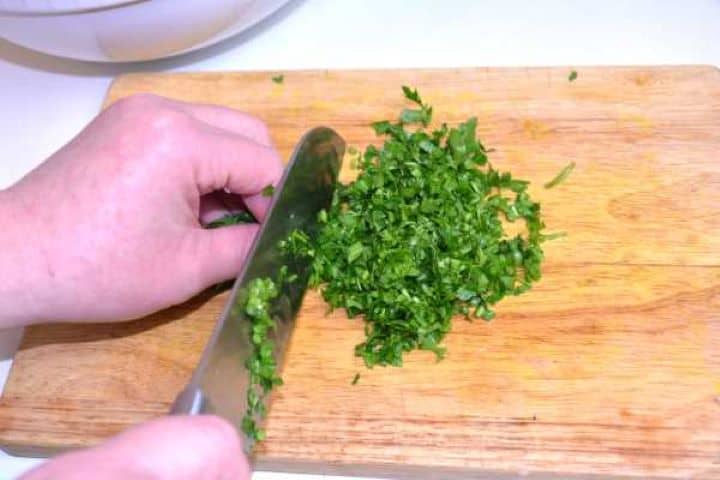 Finely chopping fresh flat-leaf parsley on a wooden board for seasoning meatloaf.