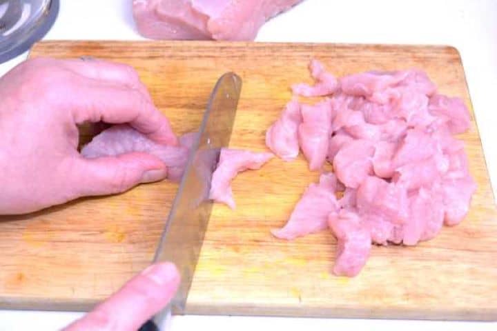 Turkey Breast Dicing raw turkey breast into cubes on a wooden cutting board before mincing.