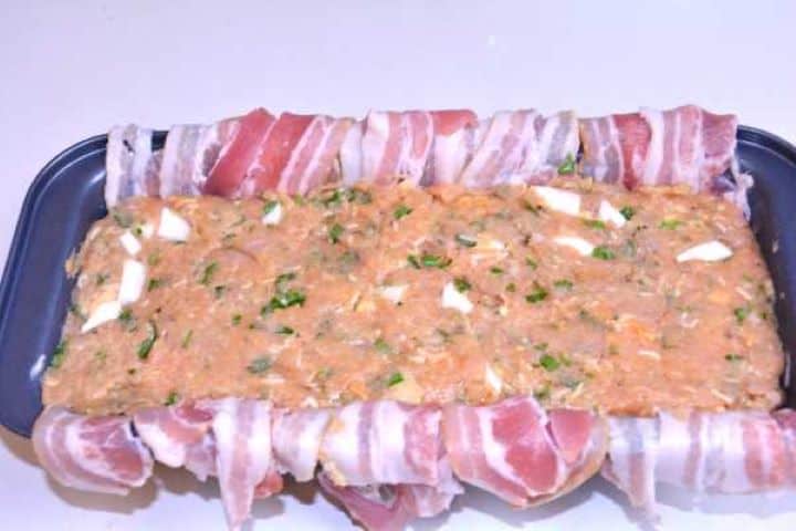 Preparing Seasoned turkey meatloaf filling pressed firmly into the bacon-lined loaf tin to avoid air pockets.