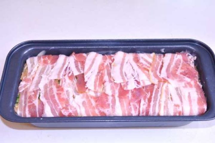 Wrapped Smoked bacon strips folded tightly over the seasoned turkey meatloaf, ready to bake.