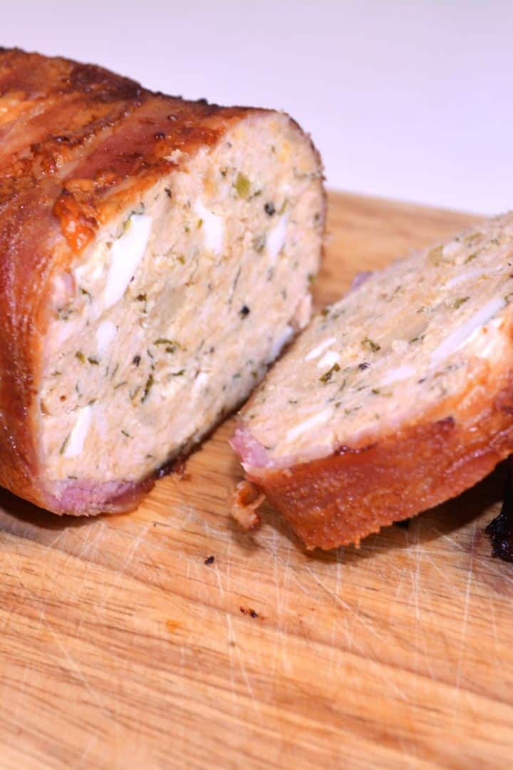 Serving Shot Sliced bacon wrapped turkey meatloaf on a wooden chopping board showing mosaic egg filling and fresh parsley.