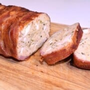 Sliced bacon wrapped turkey meatloaf on a wooden chopping board showing mosaic egg filling and fresh parsley.