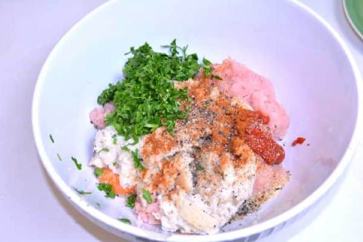 Seasoning Minced turkey in a bowl topped with milk-soaked bread panade, raw egg, grated cheddar cheese, and paprika.