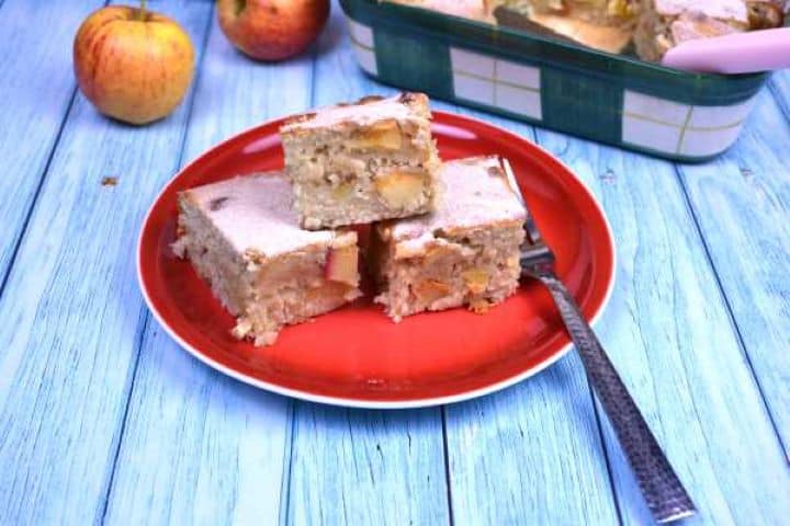 Three slices of warm cinnamon apple cake bars served on a plate dusted with icing sugar.